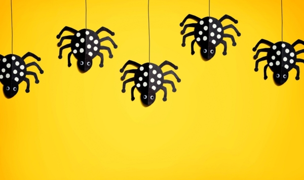 schwarze selbst gebastelte Spinnen hängen auf einem Seil auf gelben hintergrund