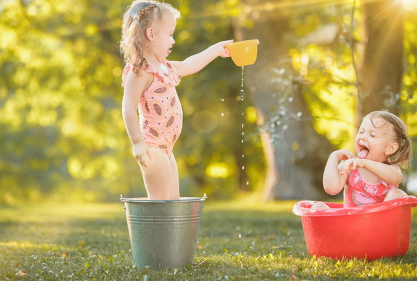 Zwei Kinder spielen im Garten mit Wasser und sitzen in Kübeln