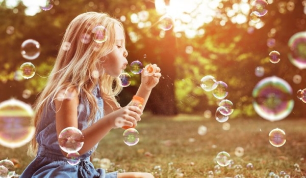 Man sieht ein kleines Mädchen, dass mit Seifenblasen spielen
